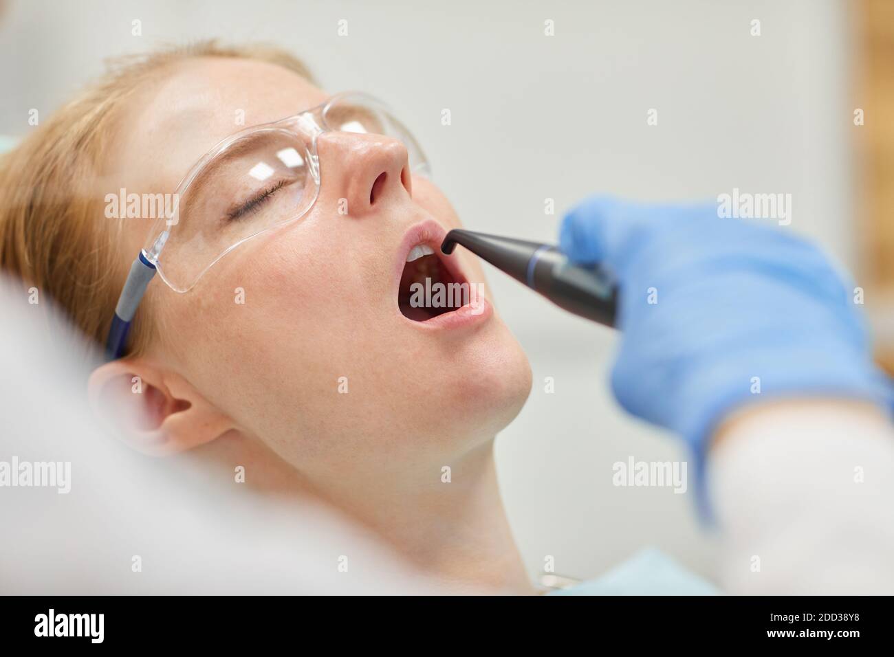 Paziente femminile in occhiali protettivi con gli occhi chiusi e. bocca aperta mentre il dentista si sta trattando i denti Foto Stock