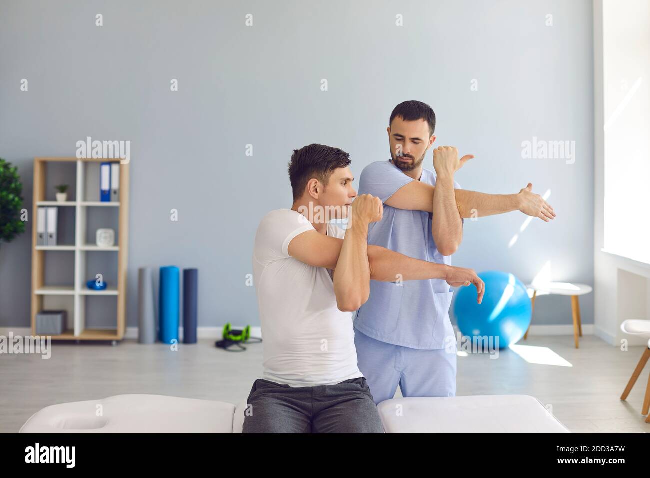 Fisioterapista che insegna al paziente di fare stiramento del corpo trasversale per alleviare il dolore e indurire la rigidità delle spalle Foto Stock