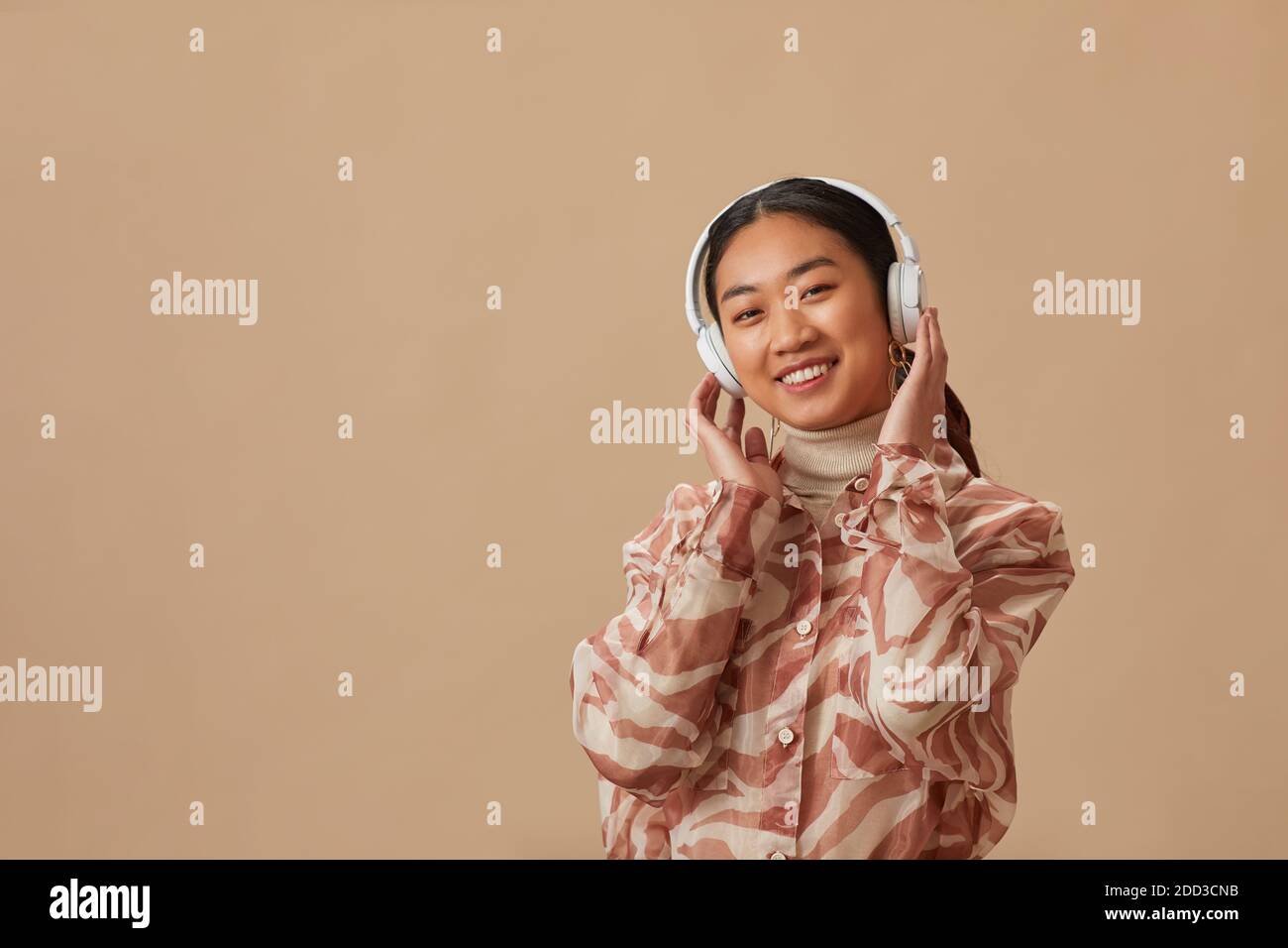 Ritratto di giovane donna asiatica in cuffie wireless che si godono musica su sfondo beige Foto Stock