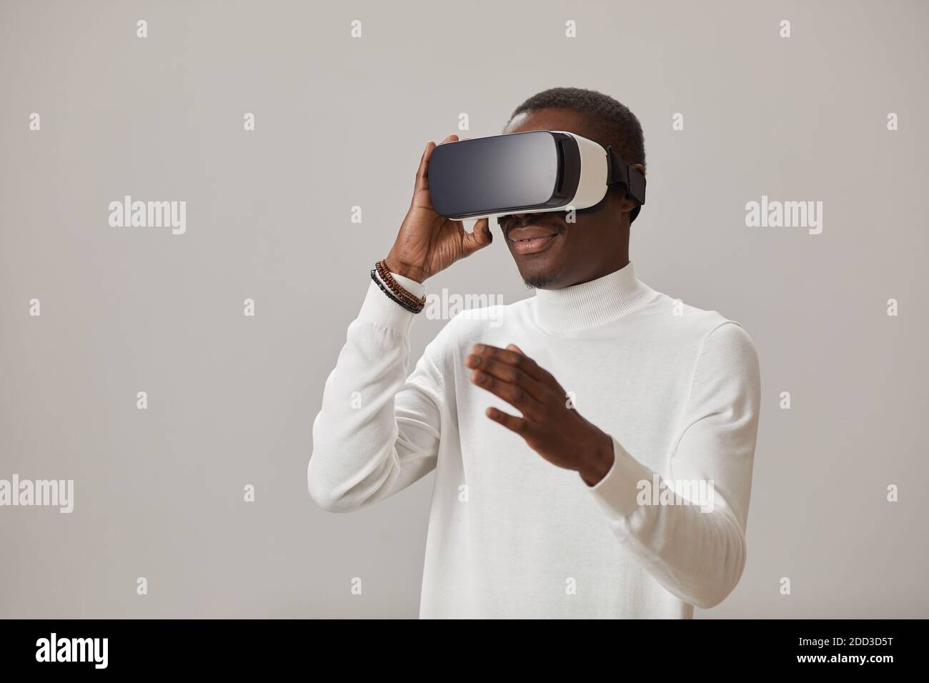 Giovane africano che indossa occhiali VR e gioca in virtuale gioco contro lo sfondo gey Foto Stock