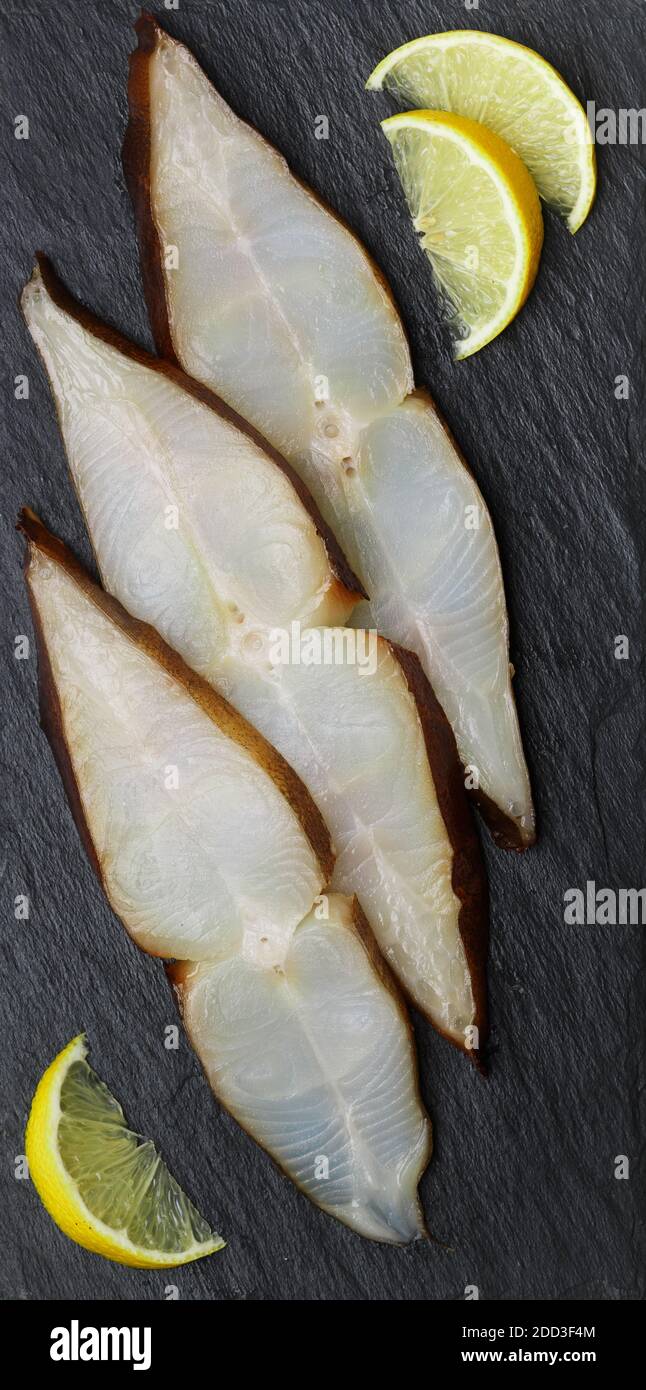 Fette di ippoglosso affumicato salato (rombo) su una piastra di ardesia nera. Un delizioso antipasto di pesce viene servito con limone. Frutti di mare. Messa a fuoco selettiva Foto Stock