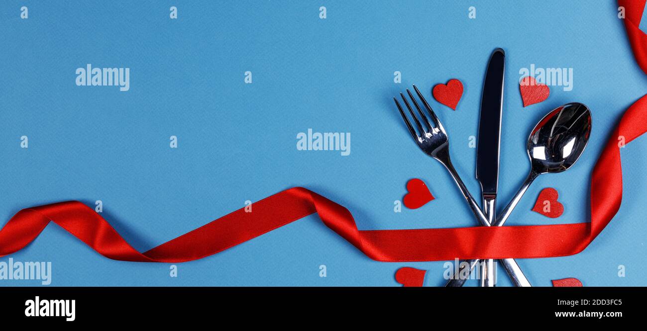 Posate legate con nastro di seta rossa e cuori Cena di San Valentino con sfondo blu Foto Stock