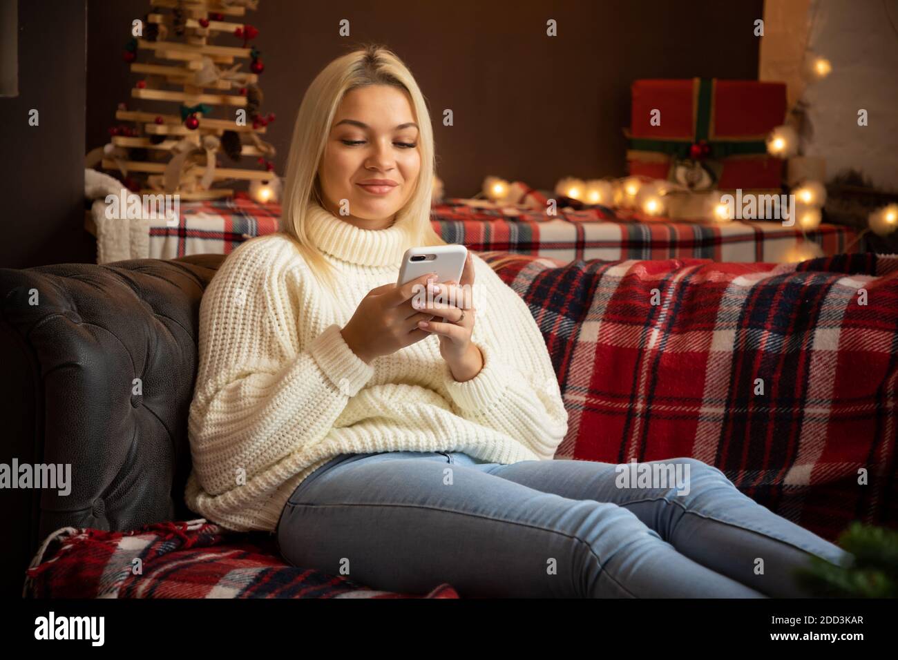 Donna felice a casa che legge un messaggio di testo mentre si siede sul divano in festa di Natale, felice anno nuovo Foto Stock