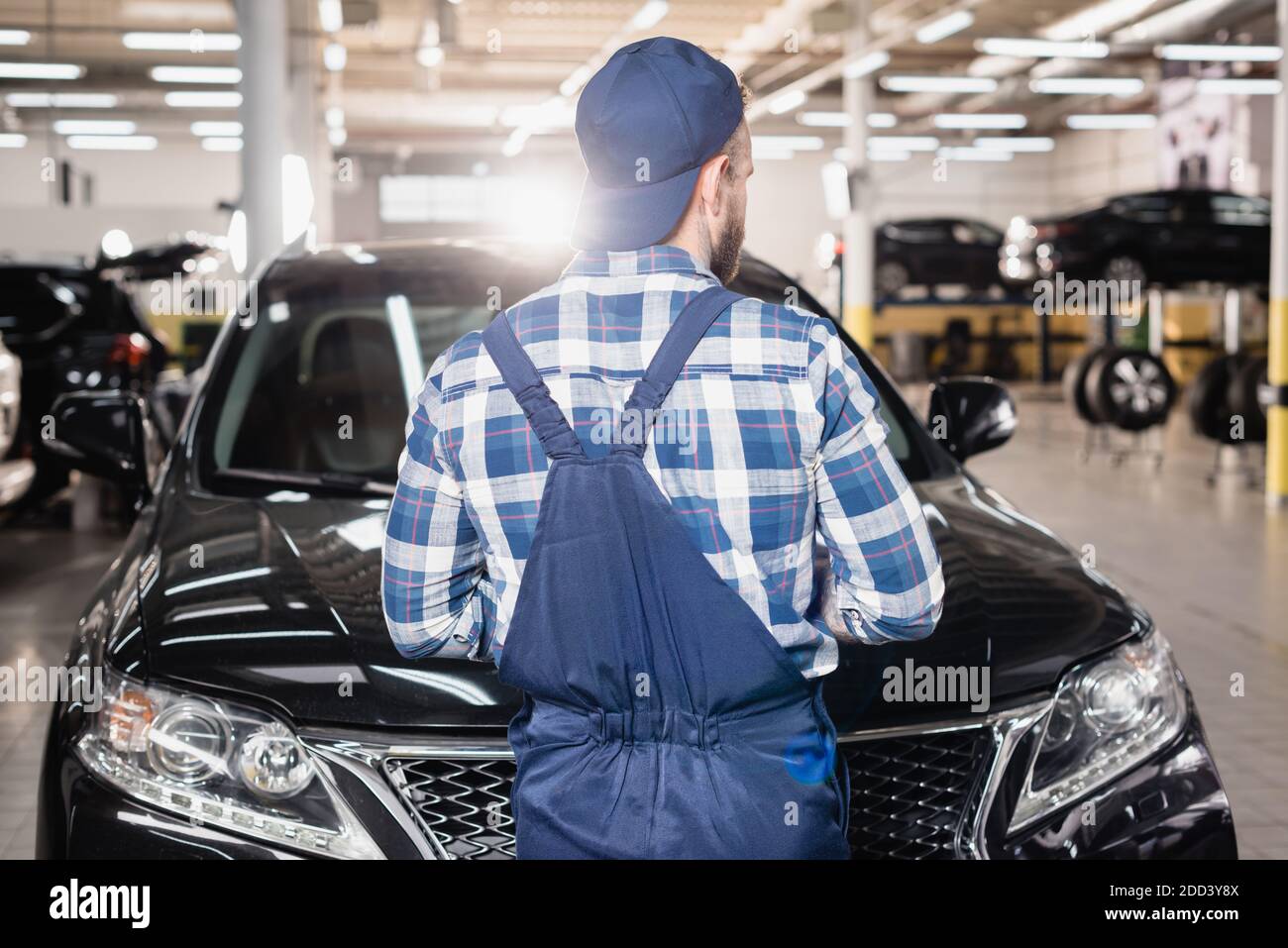 vista posteriore del meccanico in tute e tappo in piedi officina vicino alle auto Foto Stock