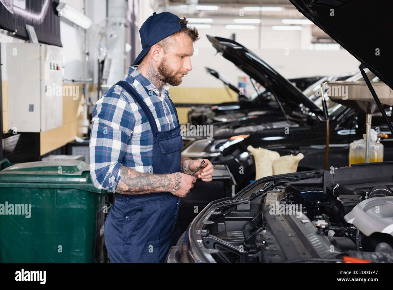 giovane meccanico in abbigliamento da lavoro in piedi vicino all'auto con  cofano aperto in officina Foto stock - Alamy