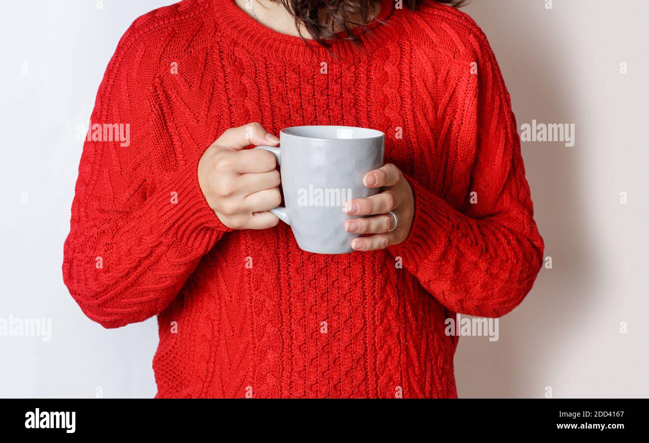 Immagine ritagliata di donna in pullover rosso che tiene la tazza grigia di tè su grigio Foto Stock