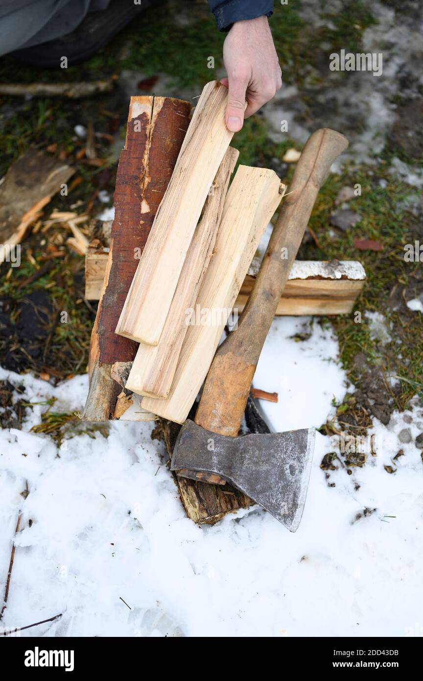 legno tritato per accendere un fuoco e un'ascia giacere a terra in inverno. una mano dell'uomo tiene un ceppo Foto Stock
