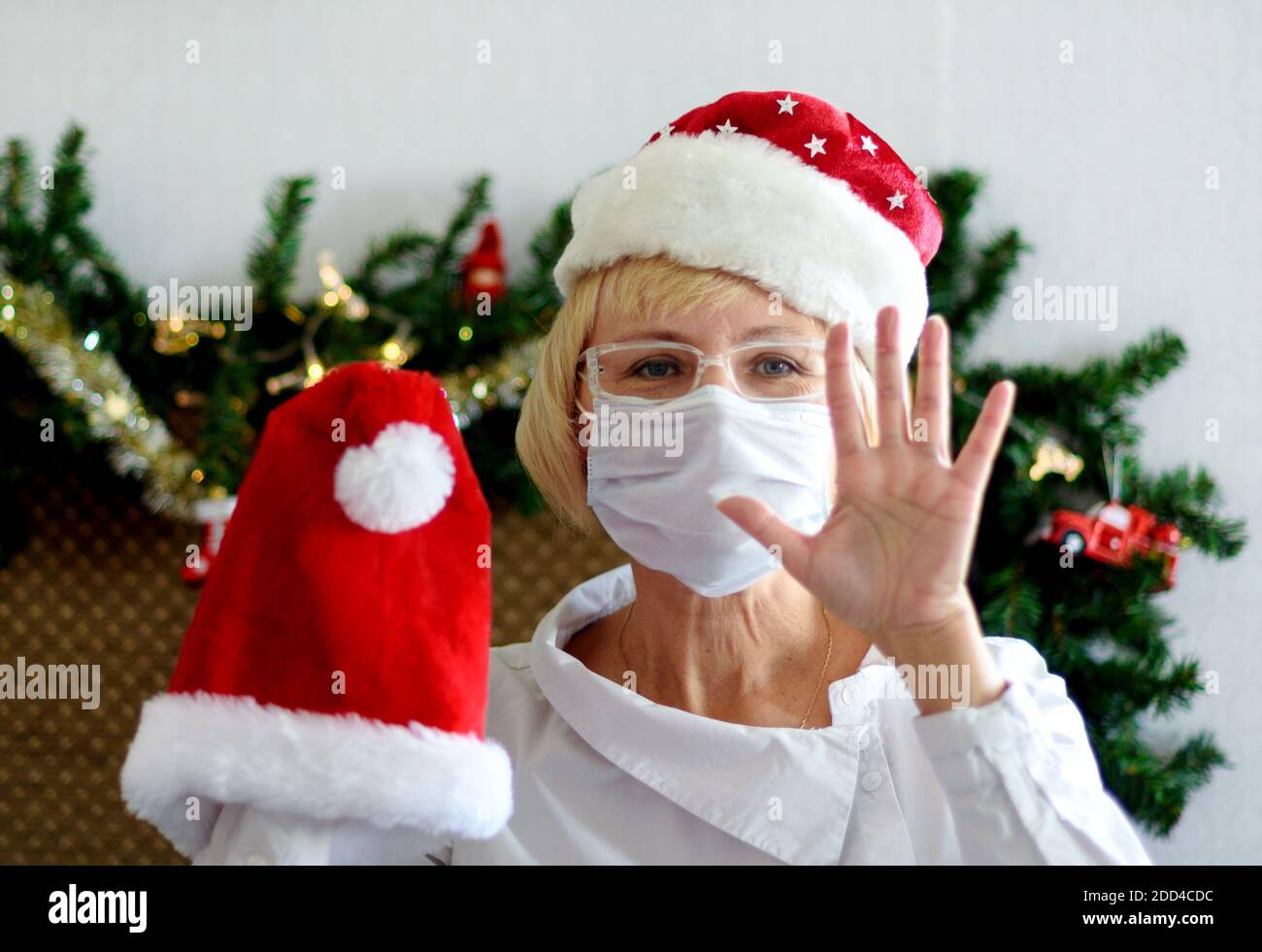 Sorridente medio - donna anziana in una maschera medica e cappello di Santa. Congratulazioni remote per Natale. Pandemia Foto Stock