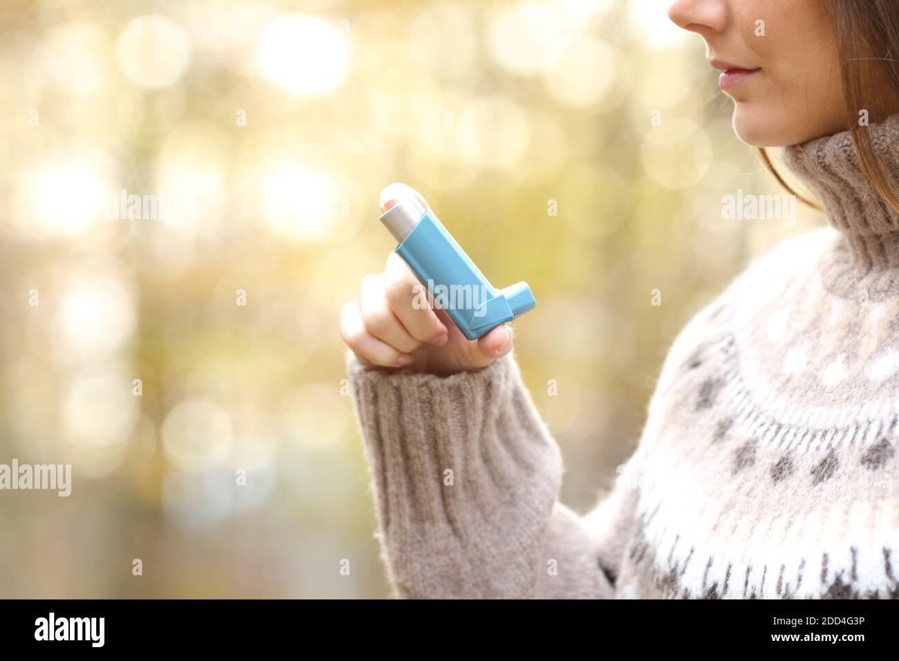 Primo piano profilo della donna che tiene a mano l'inalatore di asma pronto da utilizzare in inverno in un parco Foto Stock