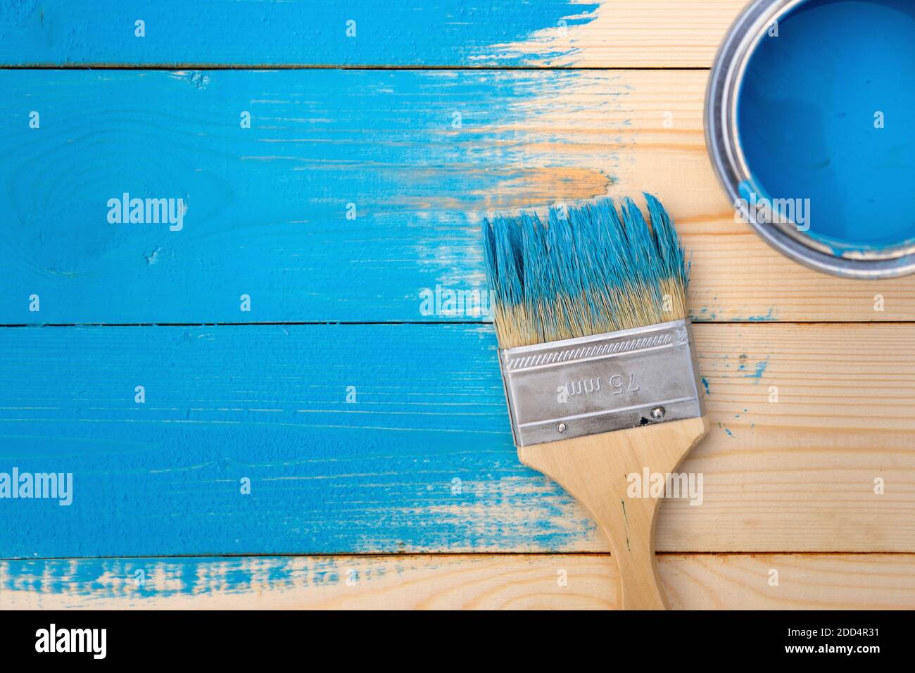 Pennello in vernice blu giace sulle tavole che non sono completamente verniciato sopra vicino ad una lattina aperta di vernice blu. Sfondo della costruzione. Vista da a. Foto Stock