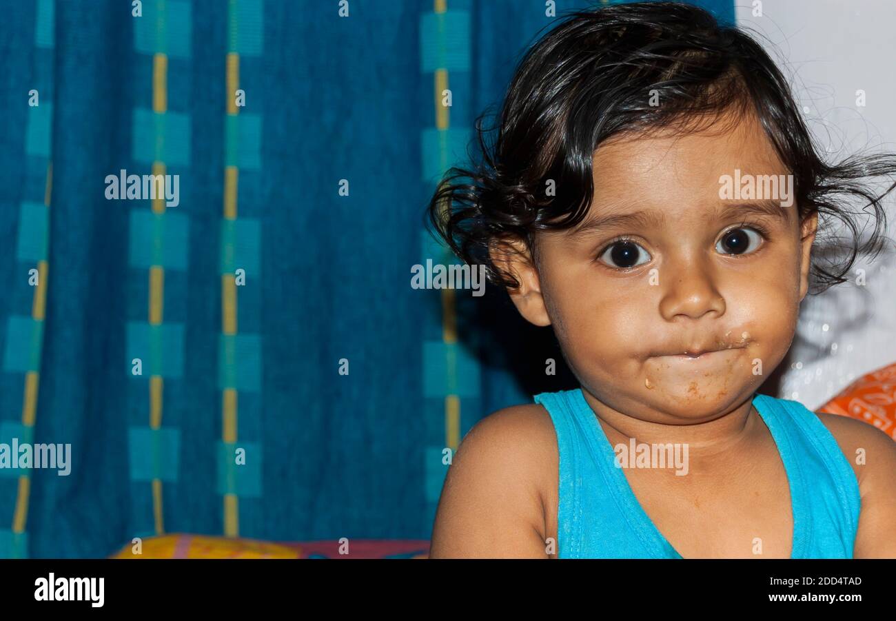 Un bambino indiano asiatico con cibo sul viso. Foto Stock