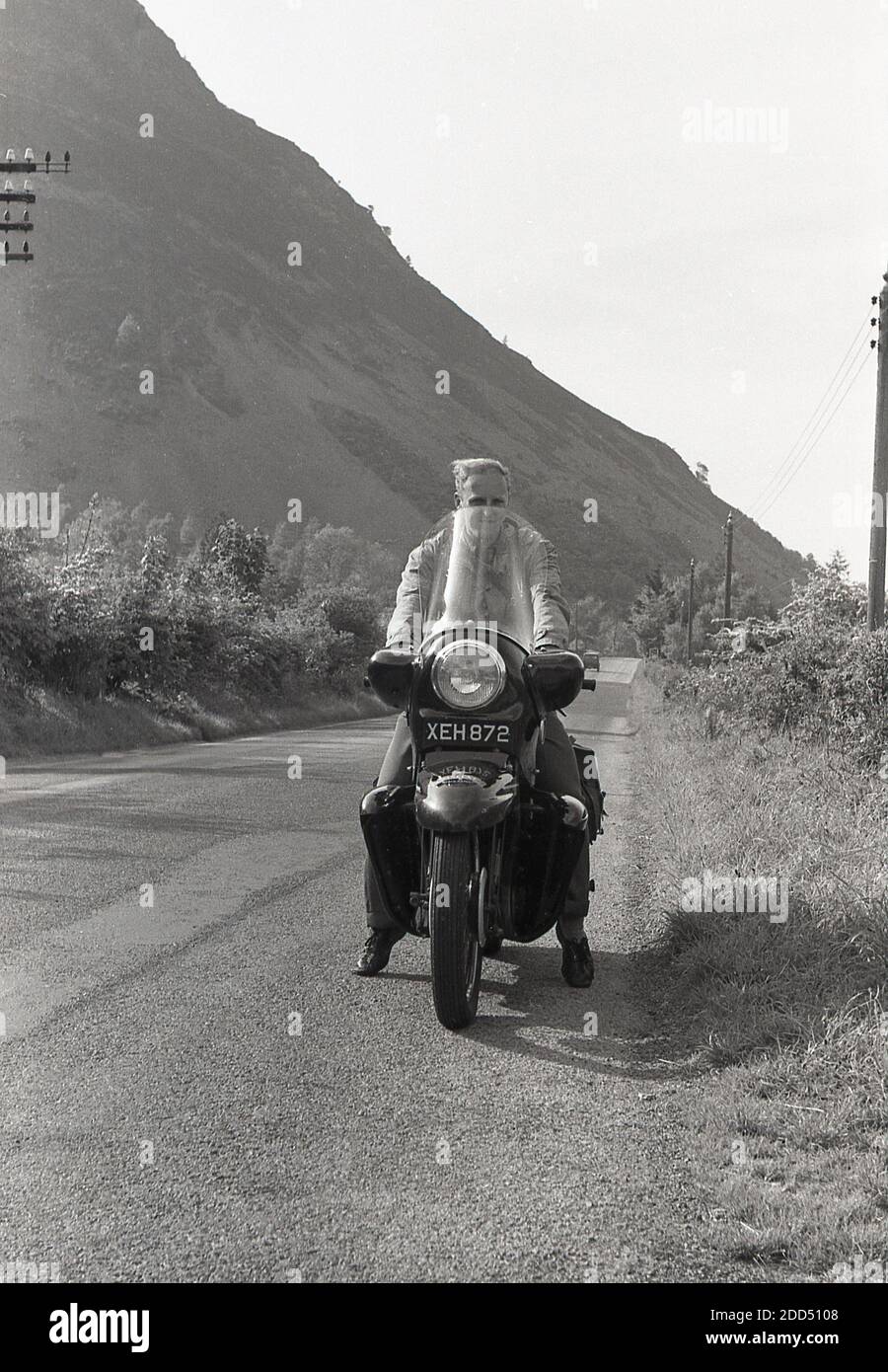 Anni '1950, storico, fuori su una strada di campagna, si fermò accanto all'erba, un uomo seduto su una moto da turismo con carenatura o parabrezza, Inghilterra, Regno Unito. Foto Stock