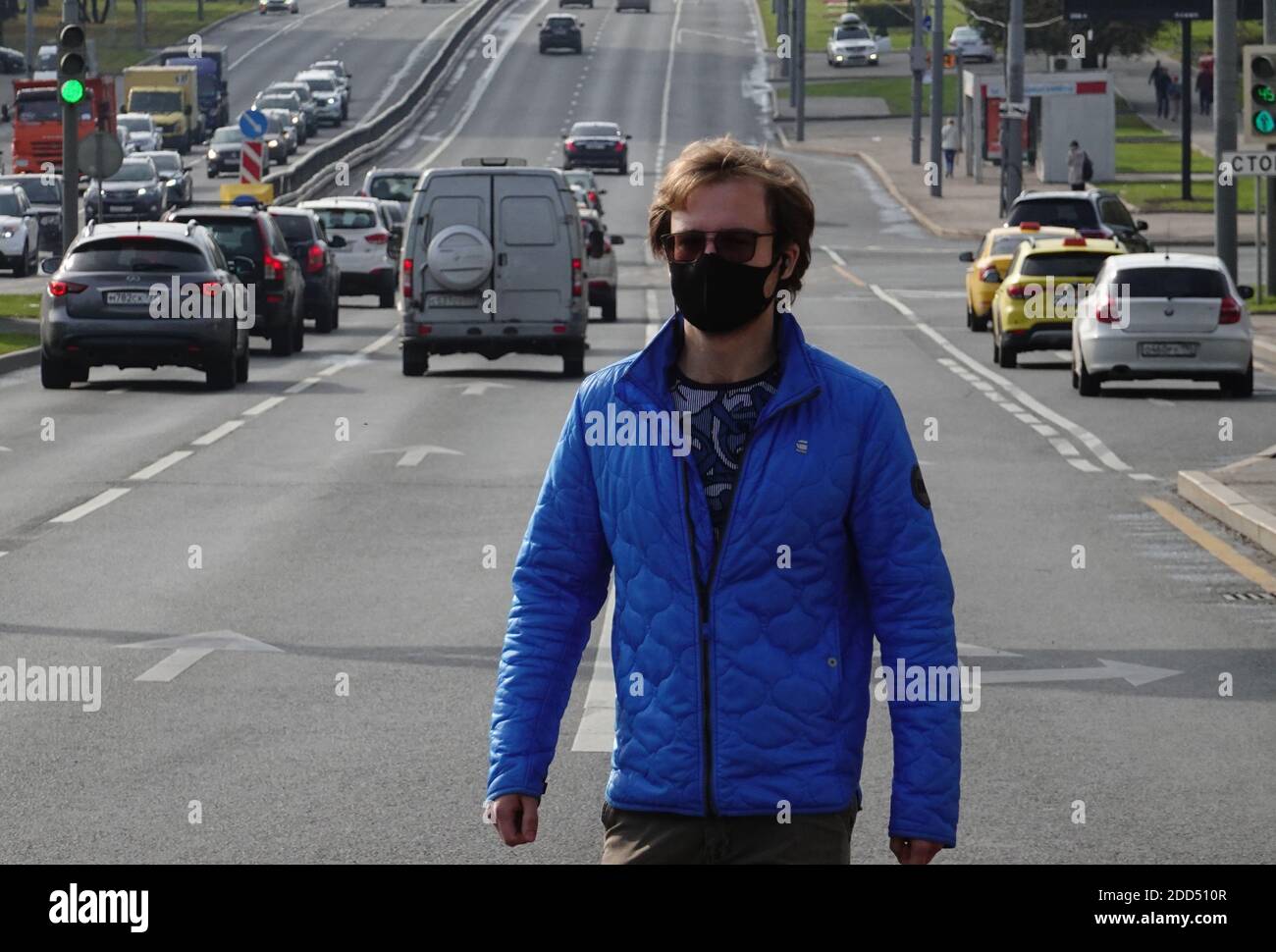 Un uomo che indossa una maschera medica COVID protettiva per la strada Foto Stock