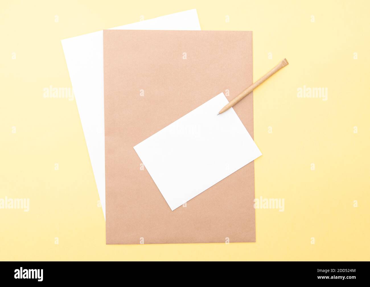 Composizione con fogli bianchi e marroni, penna su sfondo giallo, layout con spazio per il testo, vista dall'alto Foto Stock