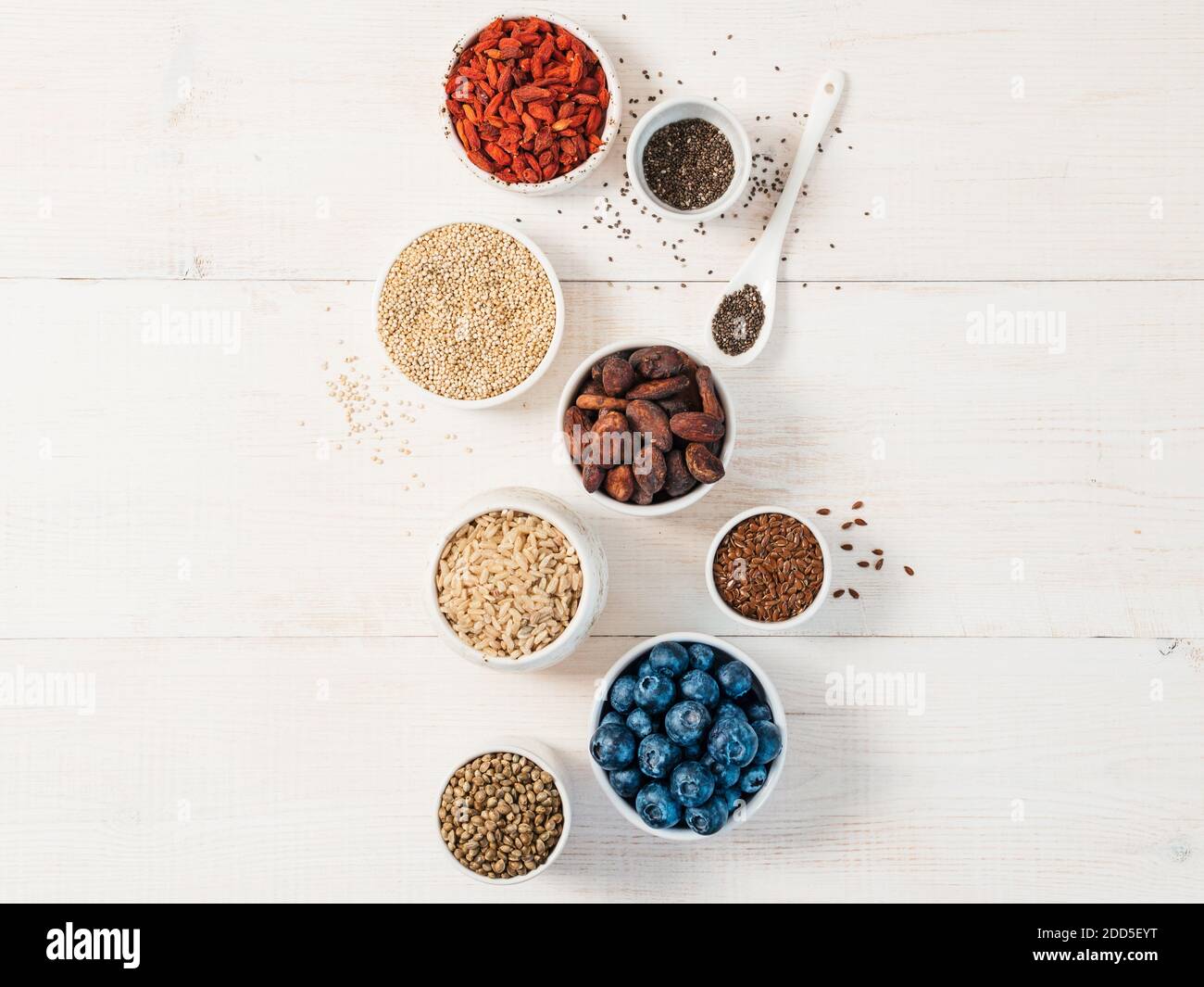 Varie superfoods in una piccola ciotola su bianco tavolo in legno.Selezione super food.Super come mirtillo, chia, materie fava di cacao, goji, sementi di canapa, quinoa, riso marrone. Copia spazio per il testo.vista superiore o laici piatta Foto Stock