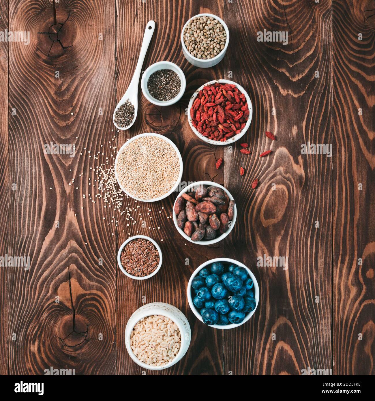 Vari superalimenti in piccola ciotola su tavola di legno.selezione super food.Superfood come mirtillo, chia, cacao crudo fagiolo, goji, semi di canapa, quinoa, riso bruno.Copy spazio per text.Top vista o piatto Lay.Square Foto Stock