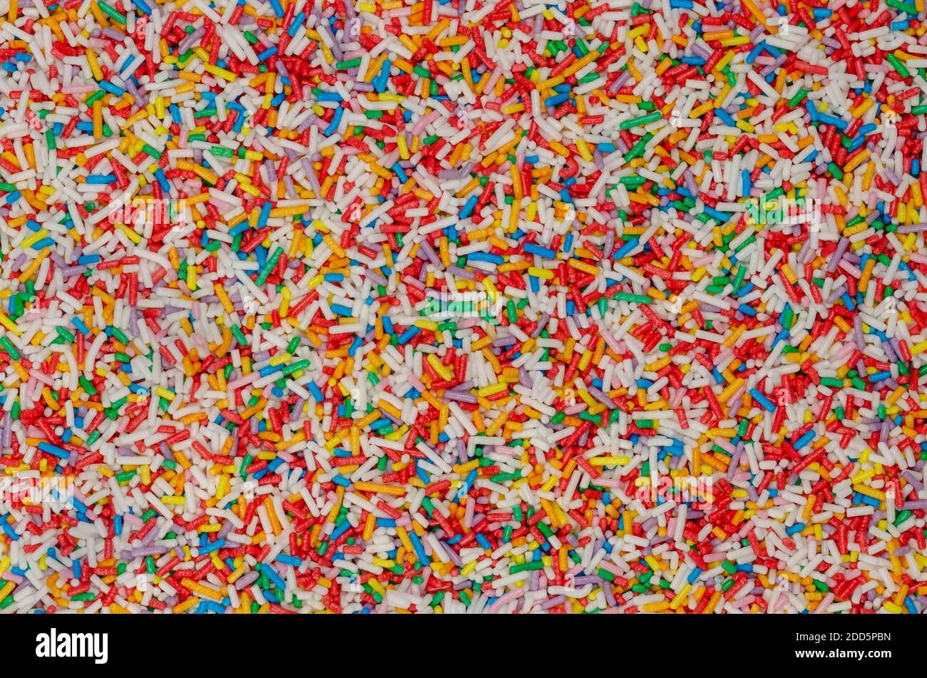 Spruzzi di arcobaleno, sfondo e superficie. Spolverare di zucchero colorato a forma di asta. Piccole caramelle in una varietà di colori, usate come decorazione o come guarnizione. Foto Stock