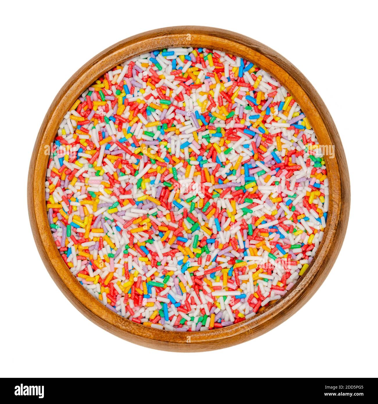 L'arcobaleno spruzza in una ciotola di legno. Spolverare di zucchero colorato a forma di asta. Piccole caramelle in una varietà di colori, usate come decorazione o come guarnizione. Primo piano. Foto Stock