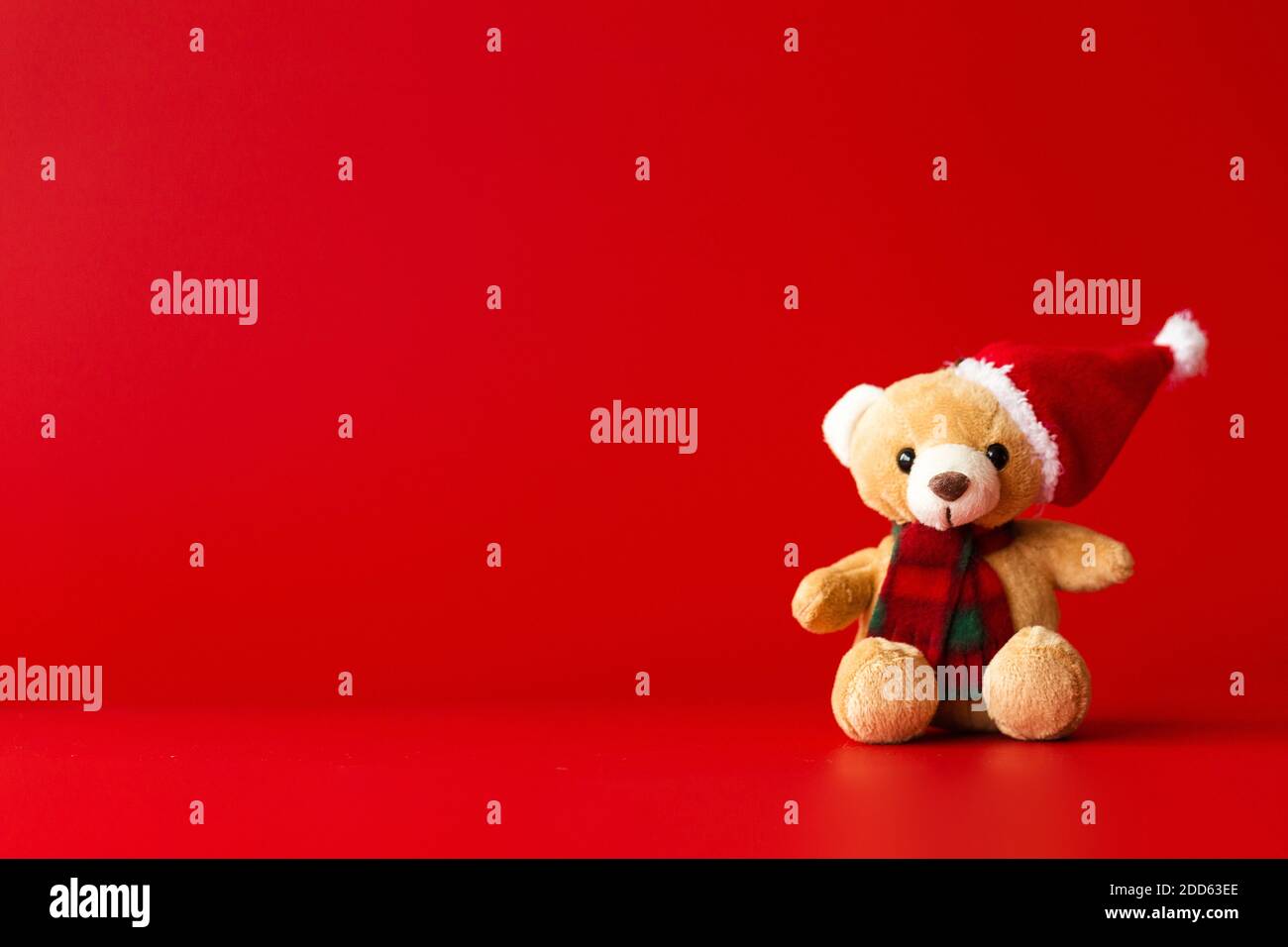 Un orso giocattolo in un cappello rosso e una sciarpa si siede su sfondo rosso Foto Stock