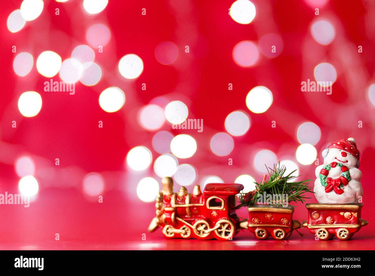 Treno a vapore giocattolo con albero di natale e pupazzo di neve in rosso sfondo con bokeh Foto Stock