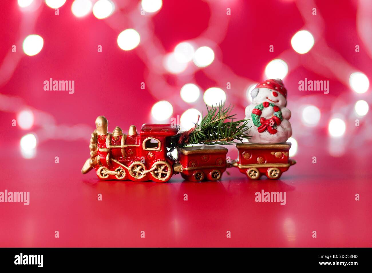 Treno a vapore giocattolo con albero di natale e pupazzo di neve in rosso sfondo con bokeh Foto Stock