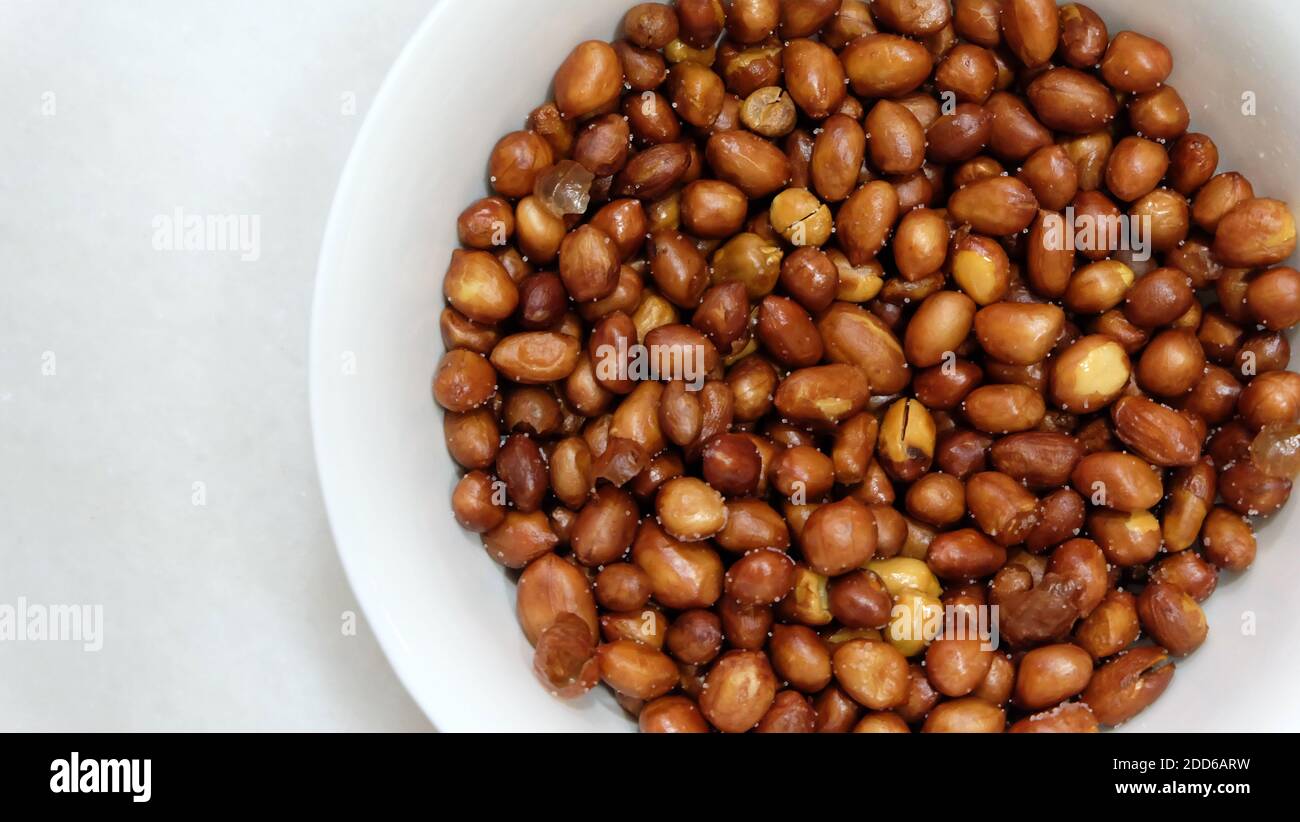 Una ciotola di arachidi fritte con la pelle, leggermente salate, in un recipiente bianco. Vista dall'alto. Foto Stock