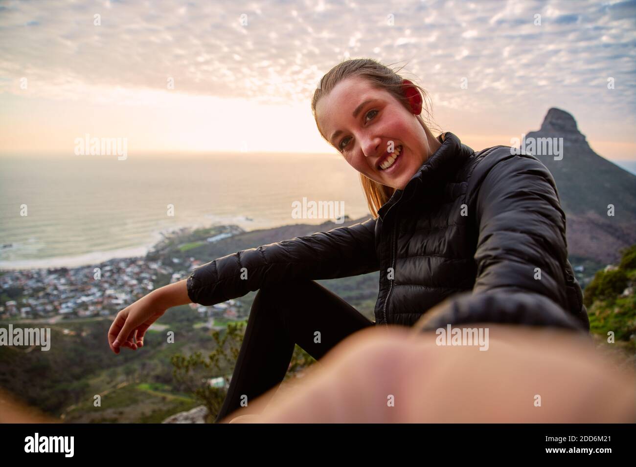 Giovane donna in vacanza con zaino che cammina lungo il percorso costiero al tramonto o all'alba prendendo selfie per postare sul sociale contenuti multimediali con telefono cellulare Foto Stock