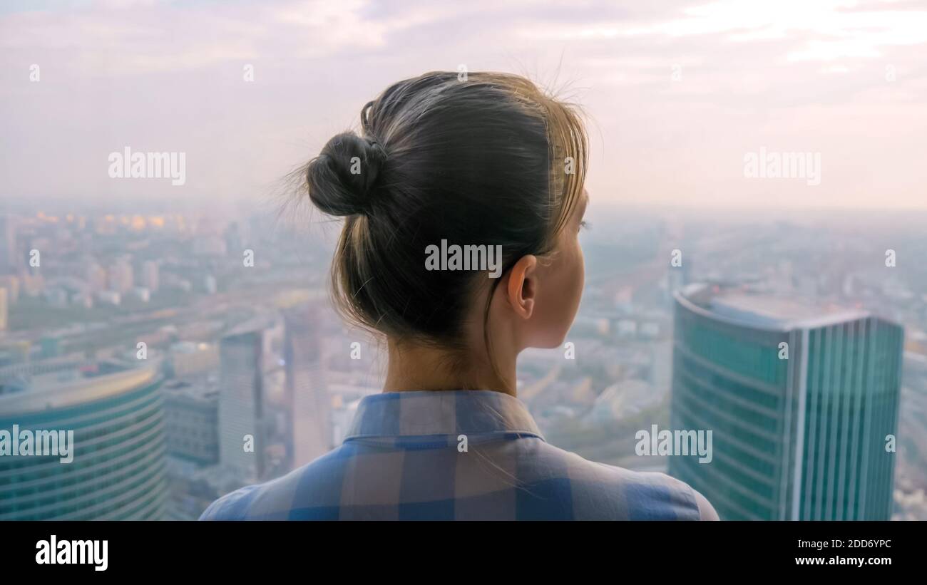 Vista posteriore di donna che guarda il paesaggio urbano attraverso la finestra di grattacielo Foto Stock