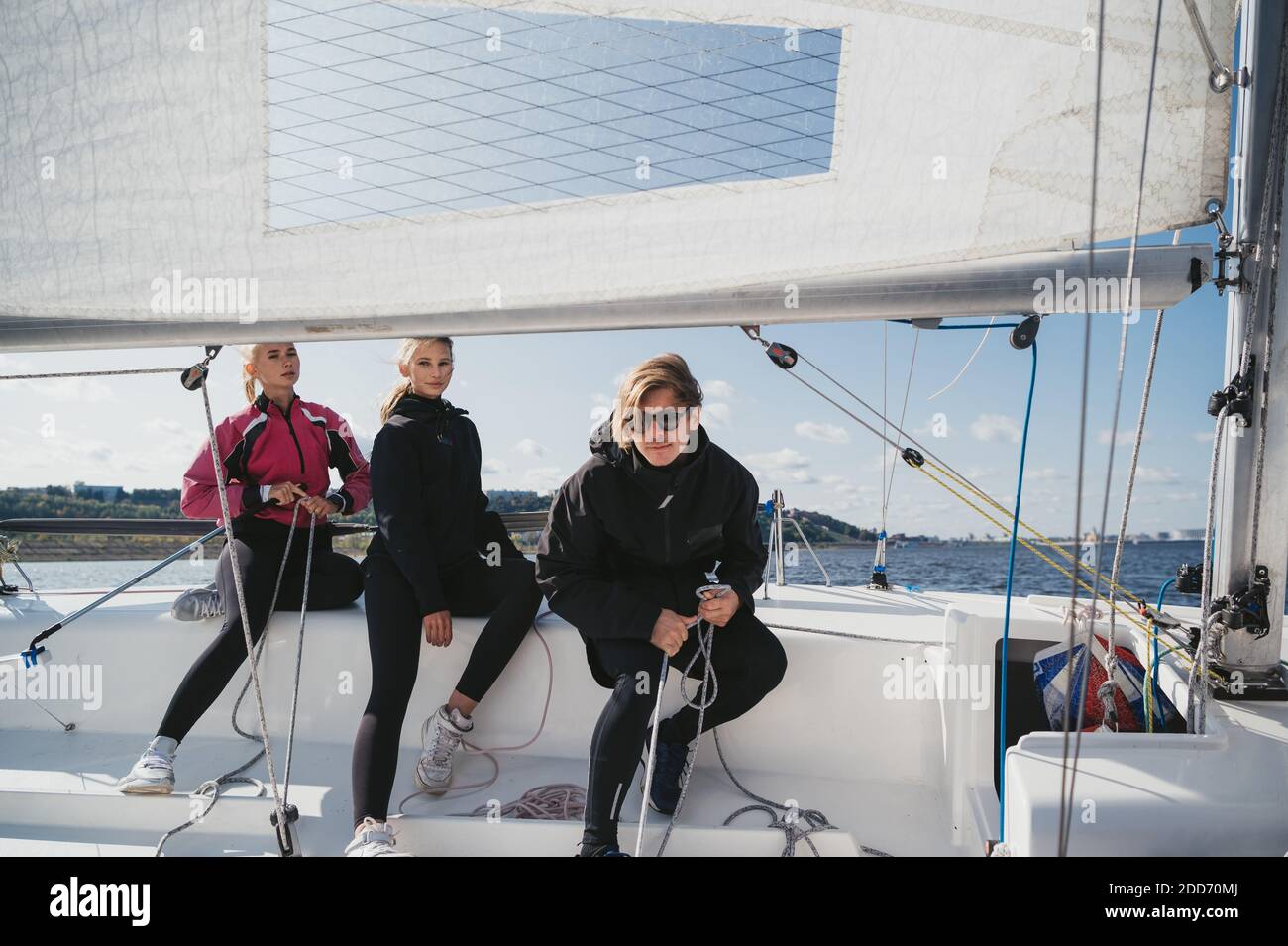 Un ragazzo giovane e due graziose ragazze si staccano dal molo su uno yacht a vela bianco per un weekend di viaggio sul lago. Foto Stock