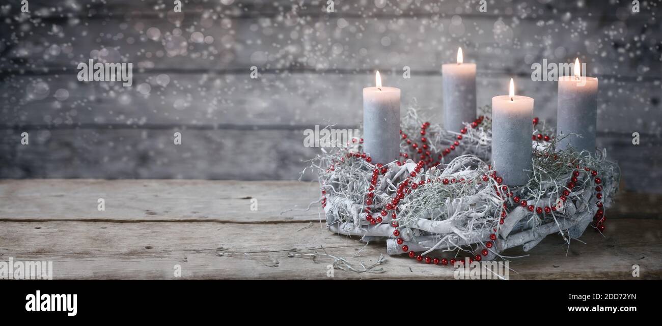 Corona di avvento di rami dipinte di bianco con candele brucianti e una decorazione a catena rossa, tradizione nel tempo prima di Natale, rustico backgro in legno Foto Stock