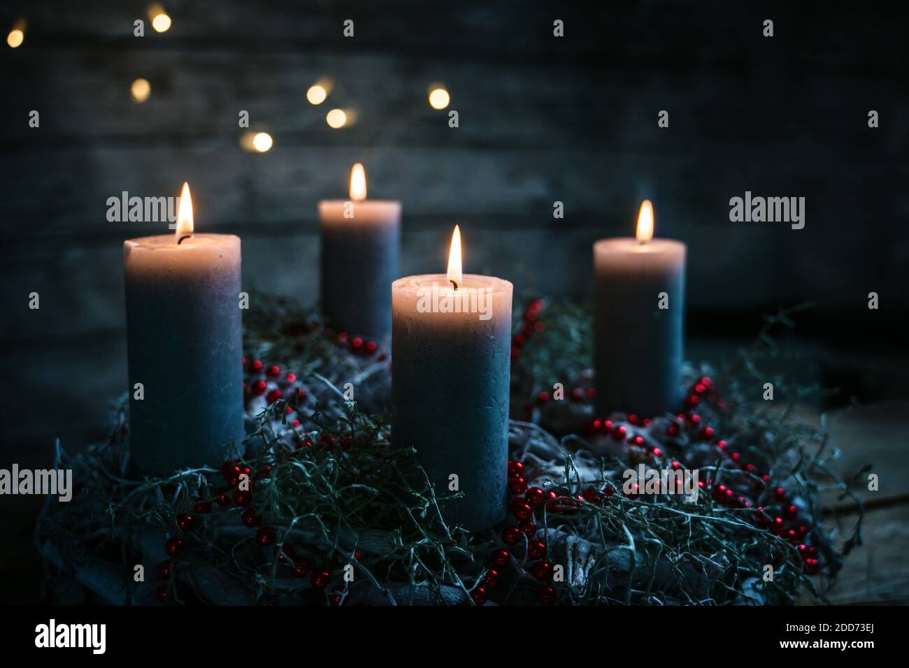Quattro candele che bruciano su una corona di avvento con decorazione di Natale rossa, tradizione di portare luce nella stagione invernale, sfondo nero rustico di legno w Foto Stock
