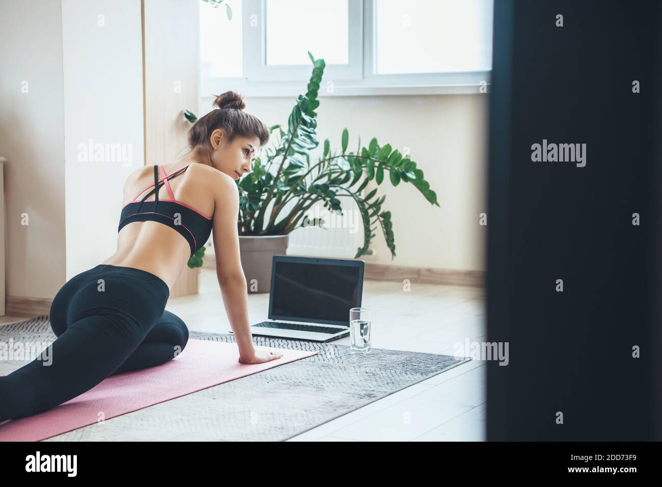 Indietro vista foto di una donna caucasica in abbigliamento sportivo avendo lezione di fitness con un computer portatile sul pavimento Foto Stock