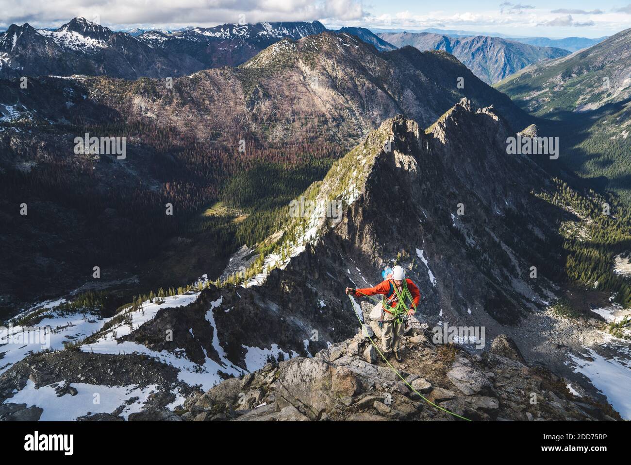 Uomo che stende la corda su roccia salita con alte montagne dietro Foto Stock