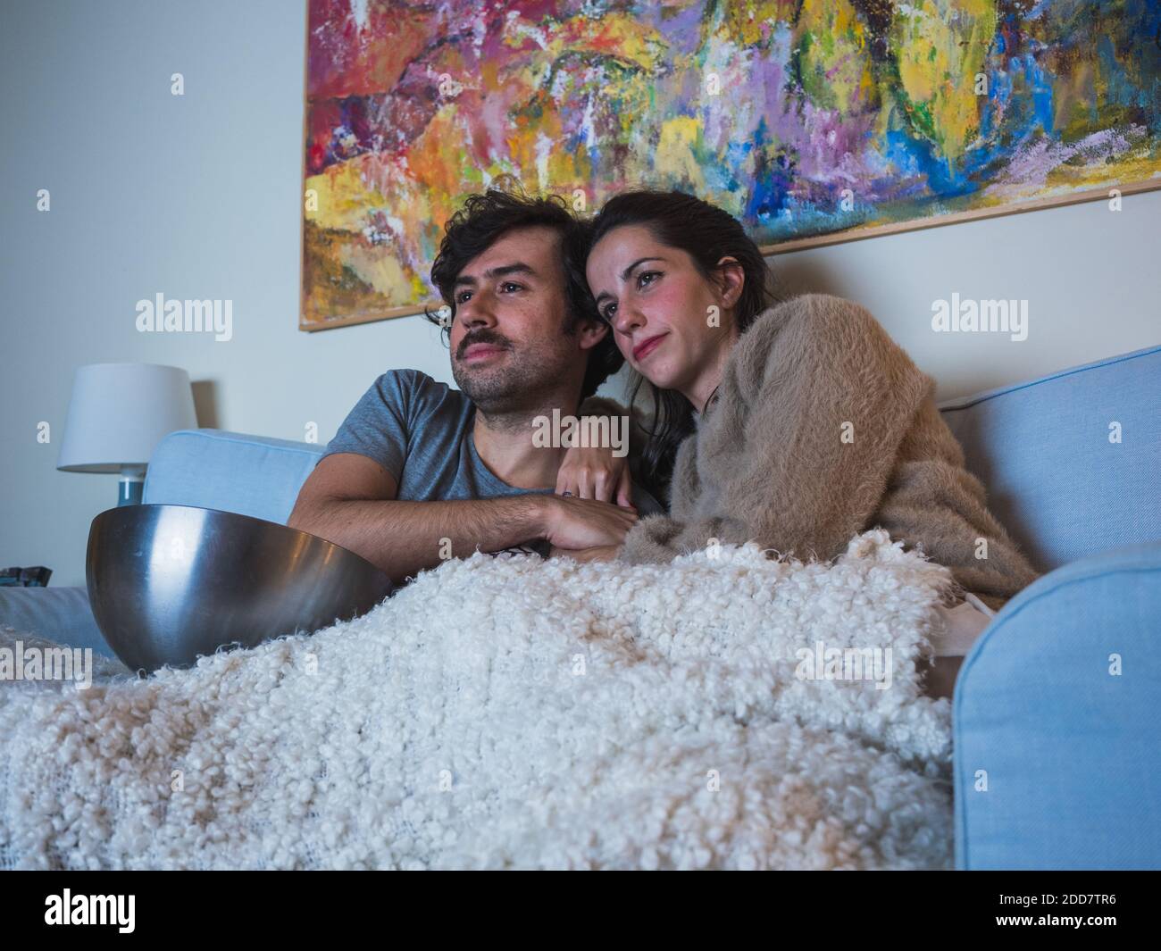 Giovane coppia sul divano a casa con coperta che guarda la televisione mangiare popcorn Foto Stock