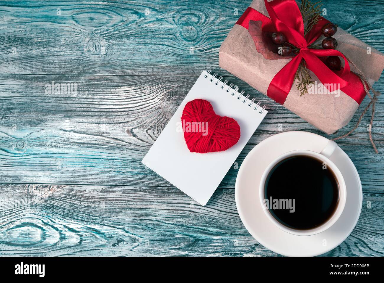Sfondo romantico e accogliente con cuore rosso, confezione regalo e tazza di caffè. Foto Stock