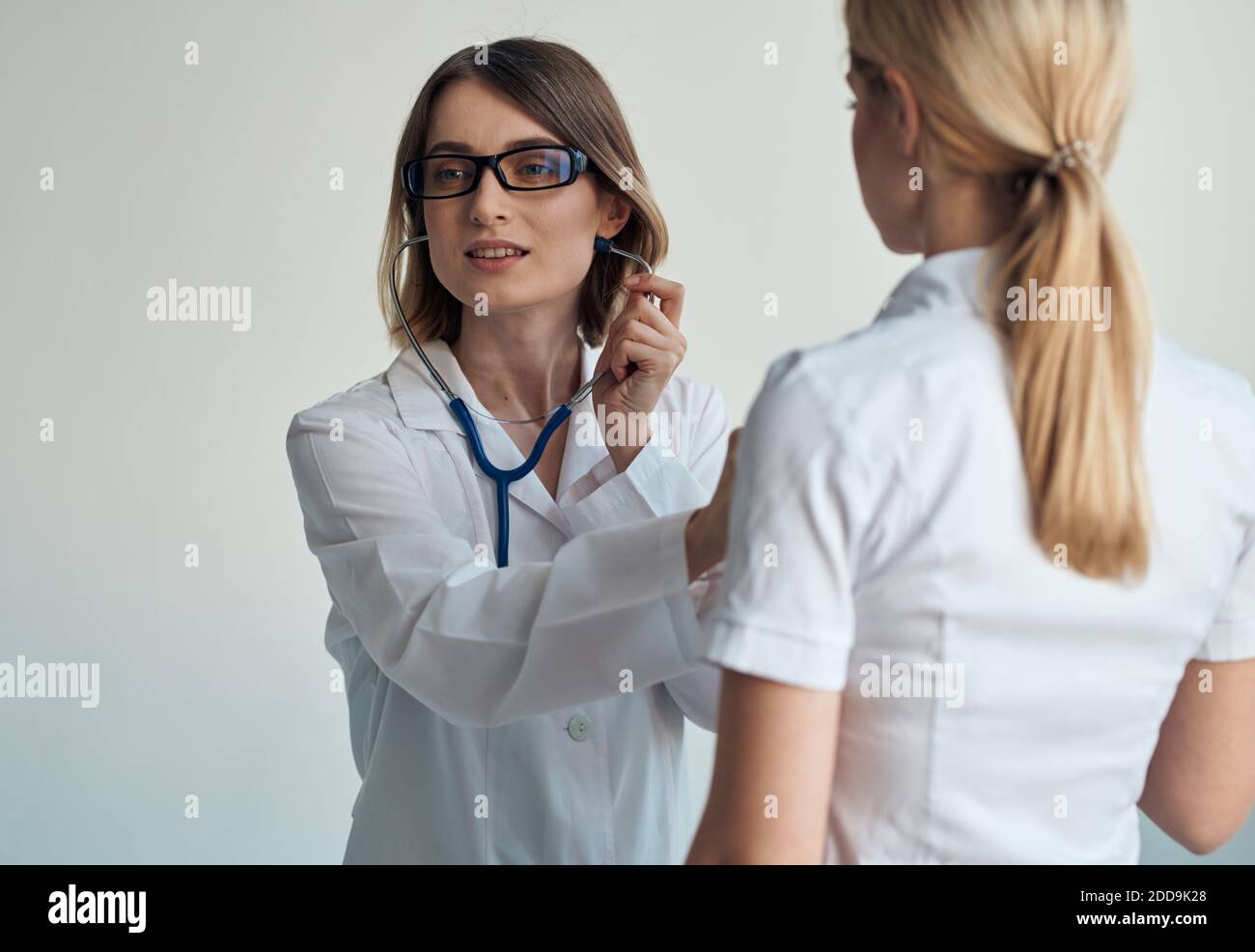 Il medico ascolta il battito cardiaco del paziente attraverso uno stetoscopio su uno sfondo chiaro vista ritagliata Foto Stock