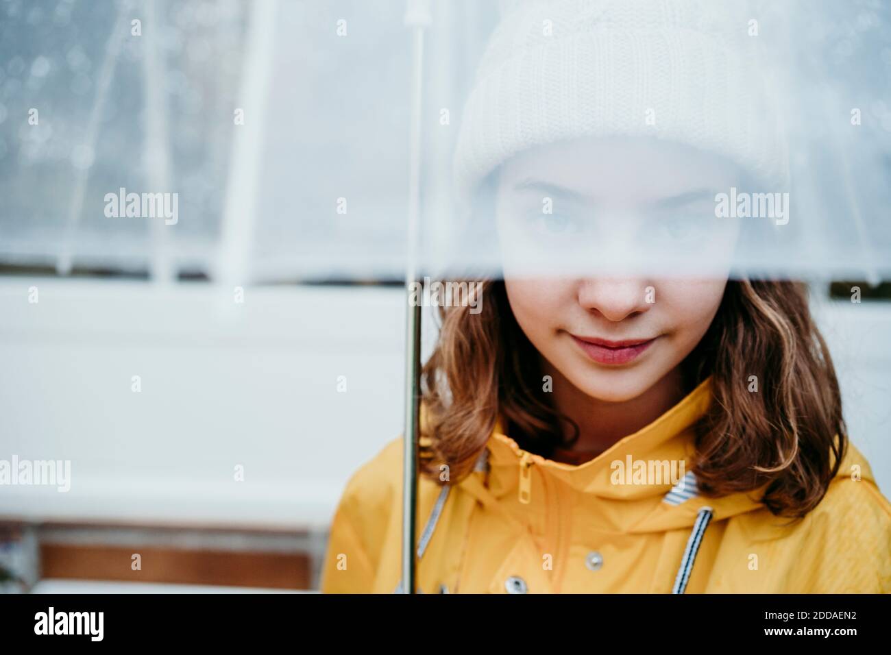 Ragazza che indossa impermeabile nascondendo faccia sotto ombrello all'aperto Foto Stock