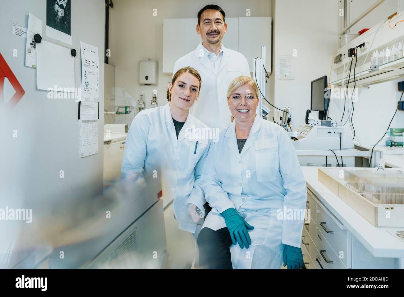 I colleghi sorridono mentre si siedono con lo scienziato in piedi sullo sfondo a. laboratorio Foto Stock