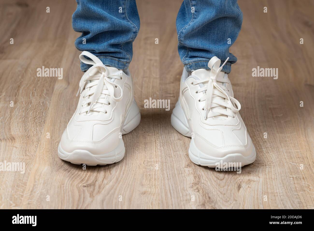 Piedi in piedi shod in bianco pizzo-up suole sneakers chunky e jeans blu sul pavimento marrone. Un paio di nuove scarpe comode per uno stile di vita attivo. Foto Stock