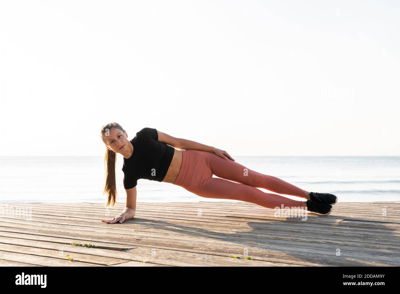 Giovane sportivo che fa la tavola laterale posa sul lungomare contro chiaro cielo Foto Stock
