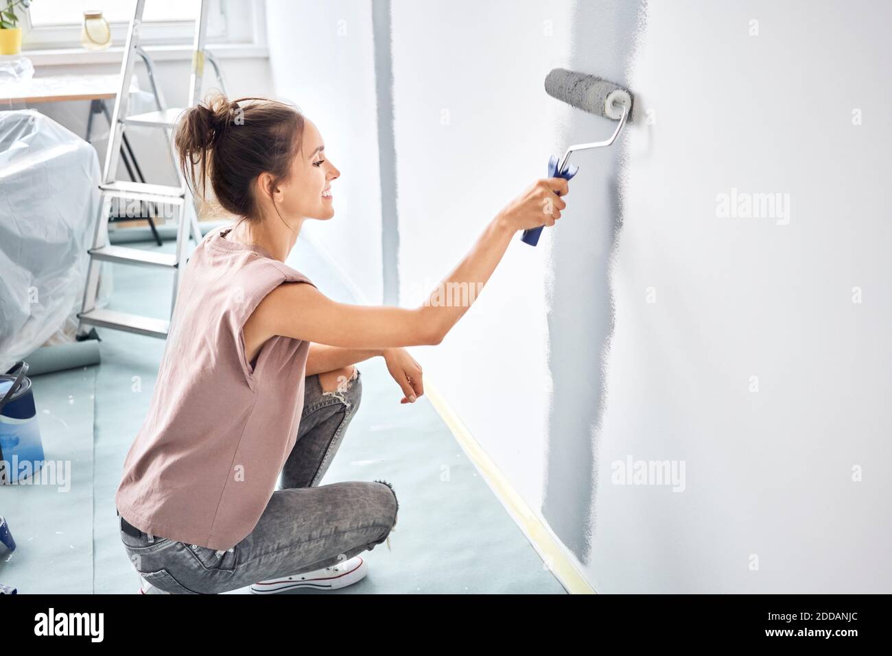 Donna sorridente pittura con rullo di vernice sulla parete mentre accovacciato a casa Foto Stock