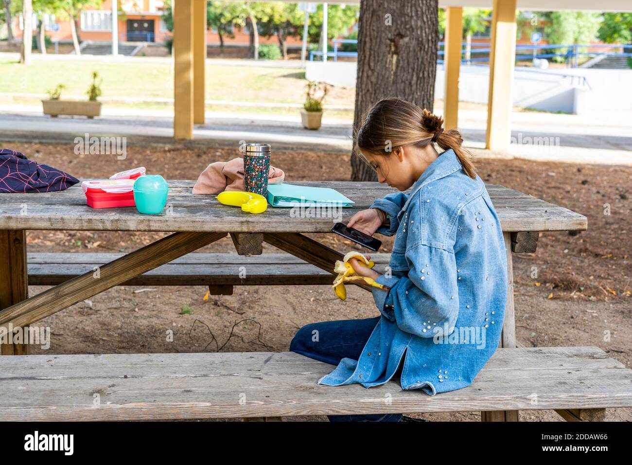 Ragazza adolescente scattando foto di banana mentre si siede sulla panchina nel parco pubblico durante la giornata di sole Foto Stock