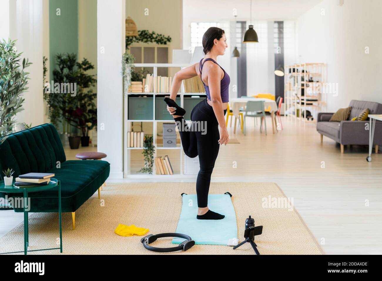 Giovane donna in piedi su una gamba di registrazione video mentre in piedi a casa Foto Stock