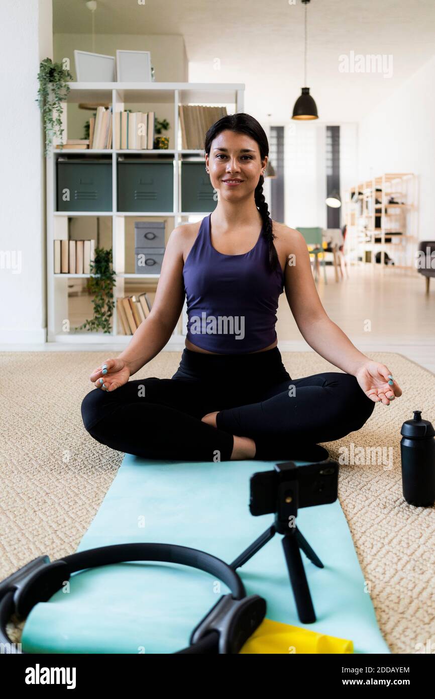Giovane donna che medita durante la registrazione video a casa Foto Stock