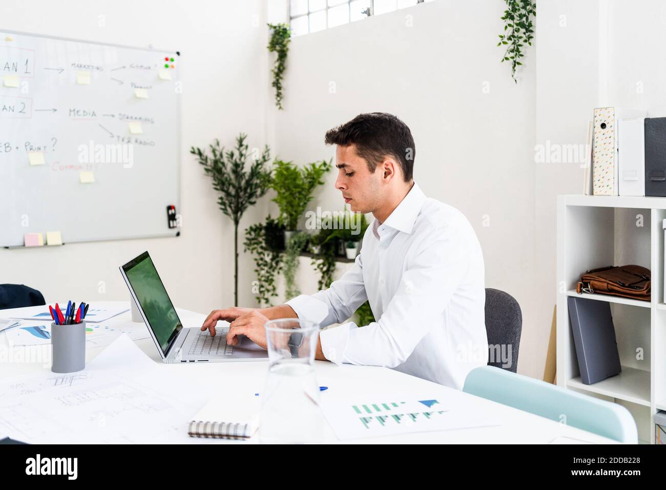 Bell'uomo d'affari che usa il laptop mentre pianifica la strategia alla scrivania dentro ambiente di lavoro creativo Foto Stock