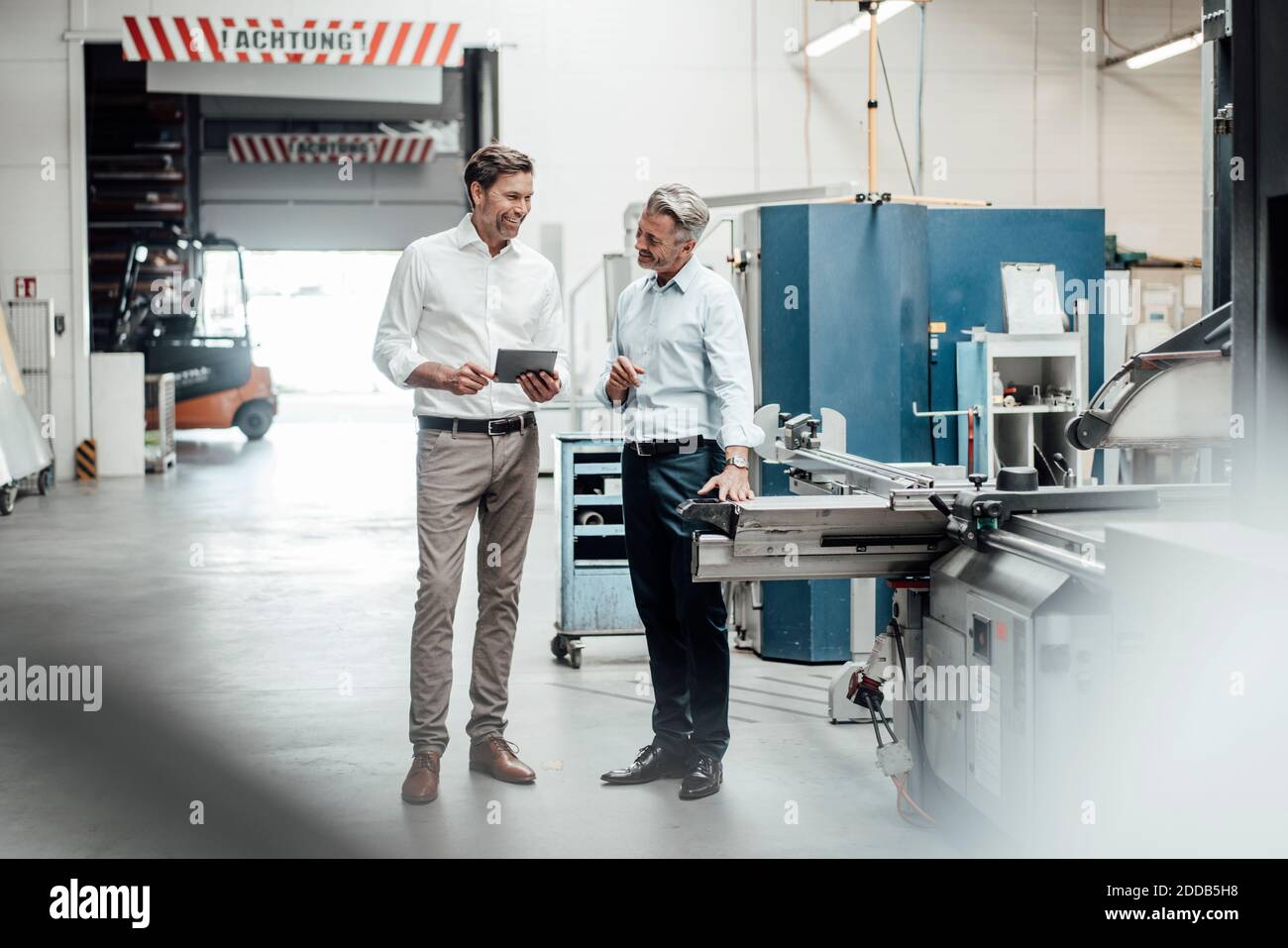 Felici uomini d'affari maturi che discutono mentre si levano in piedi in fabbrica Foto Stock
