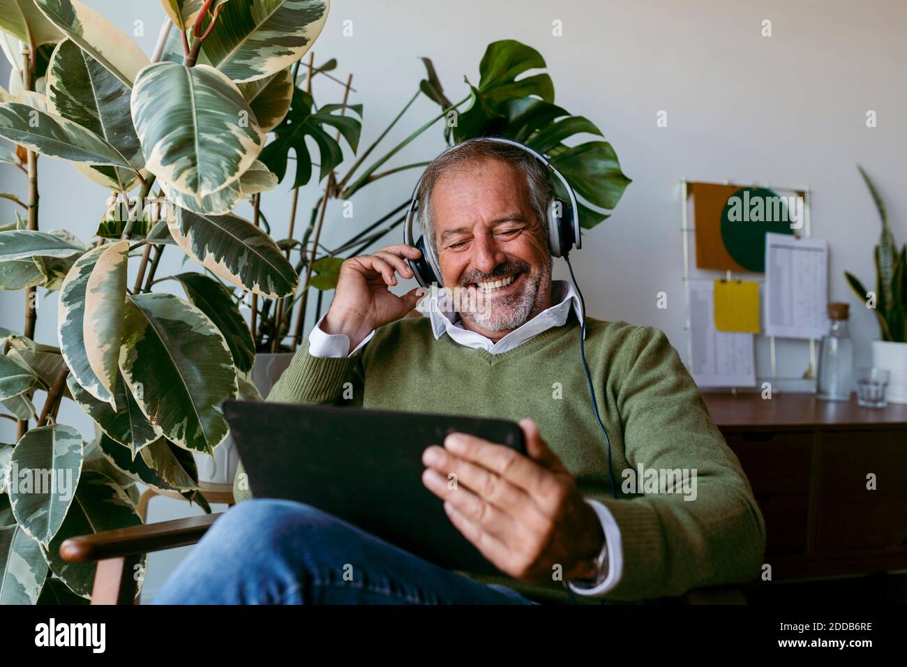 Uomini sorridenti e maturi che indossano le cuffie mentre usano il tablet digitale AT casa Foto Stock