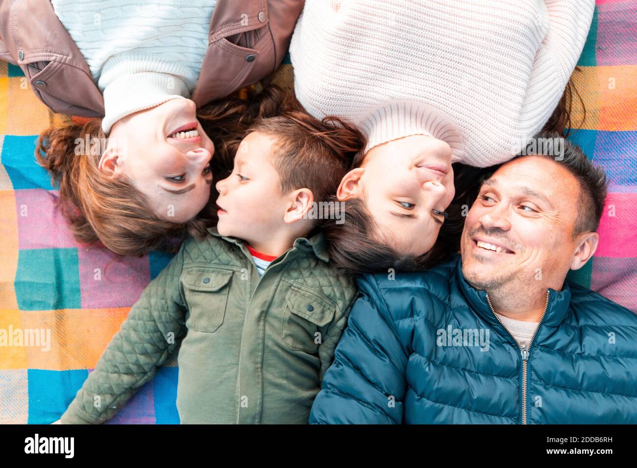 Direttamente sopra la vista di una famiglia sorridente che si guarda l'un l'altro mentre sdraiato su coperta da picnic nel parco Foto Stock