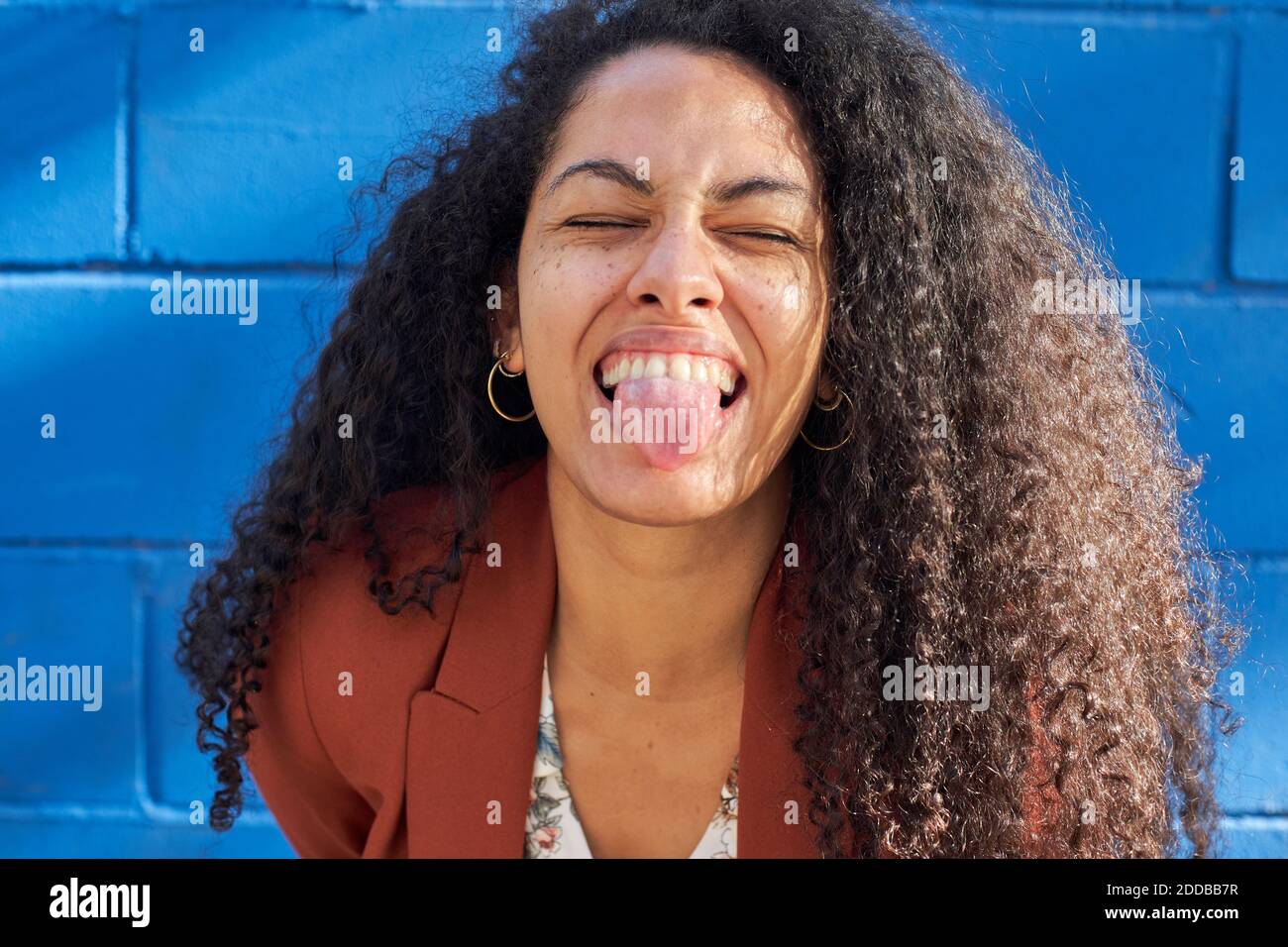Donna che si stacca la lingua contro la parete blu nella giornata di sole Foto Stock