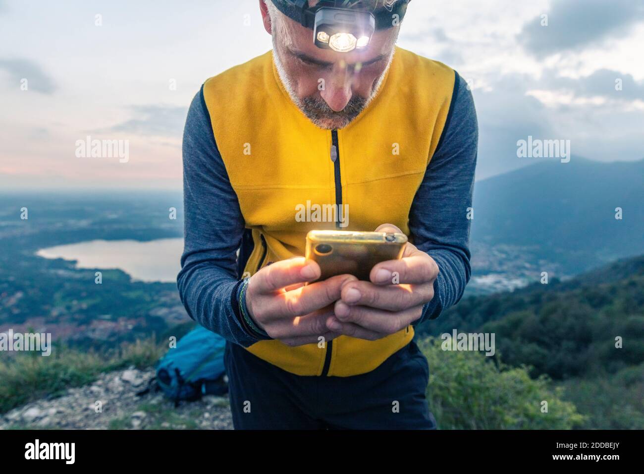 Escursionista maschile maturo che utilizza smartphone mentre si sta in piedi contro il cielo al tramonto Foto Stock